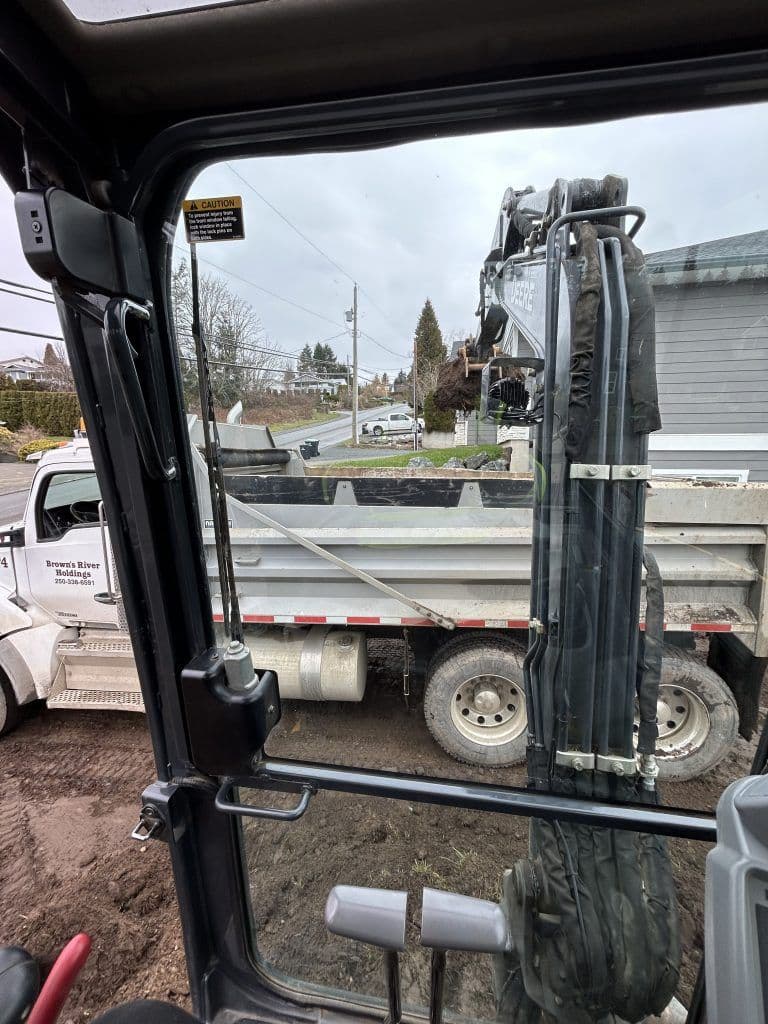 View from an excavator cab showing a dump truck and construction site.