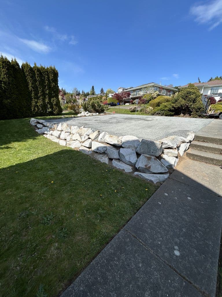 Landscaped yard with a rock retaining wall, stone pathway, and blue sky background.