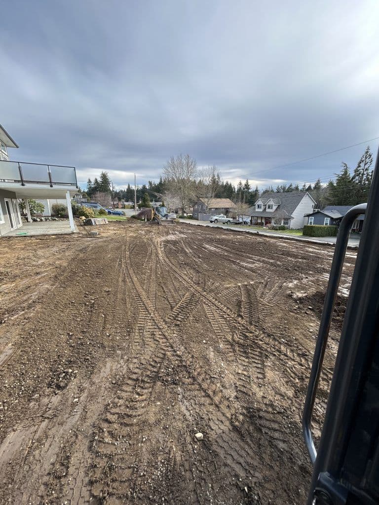 Construction site showing freshly graded dirt area and cloudy sky in residential neighborhood.