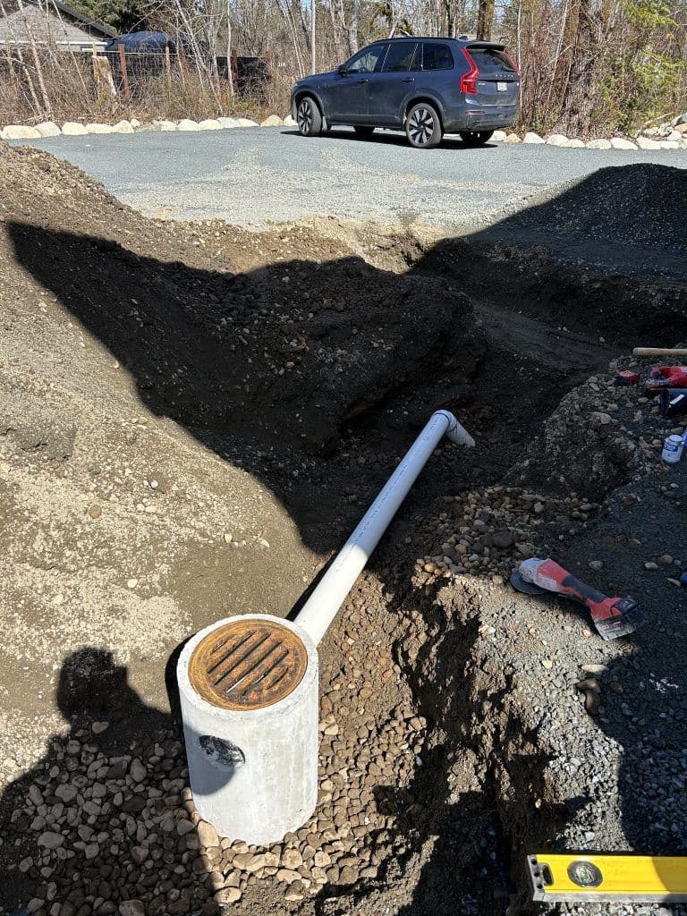 Excavated area with a drainage pipe and gravel, car parked in the background.