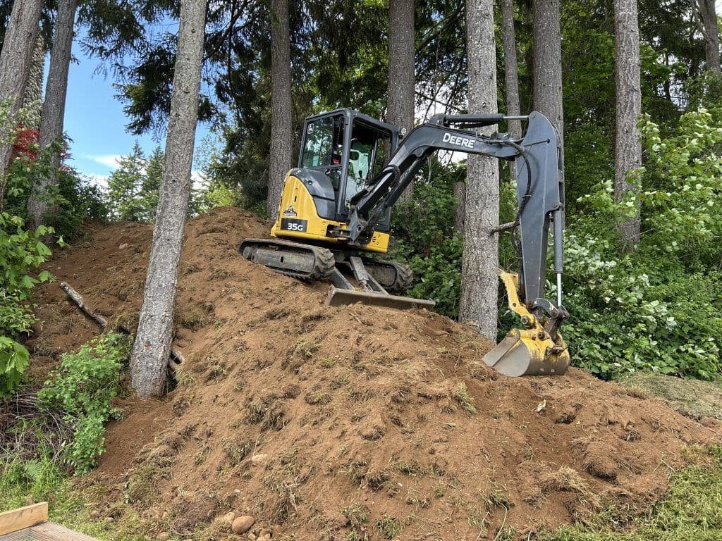 Excavator on a hillside surrounded by trees, preparing land for construction.