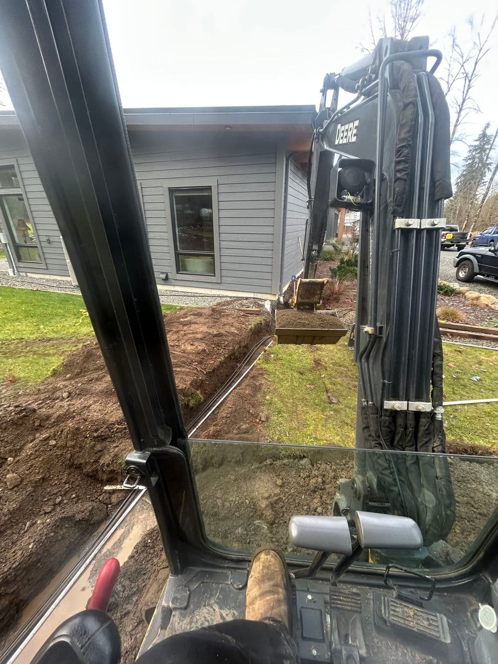 Excavator digging trench near modern home for utility installation.