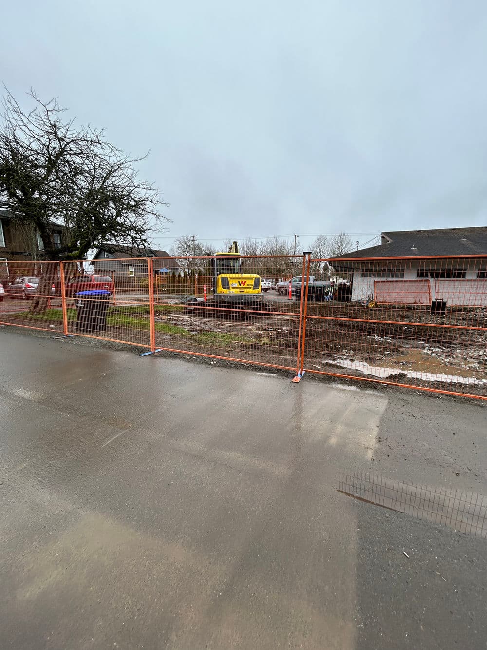 Construction site with a fenced area, featuring heavy machinery and nearby residential buildings.