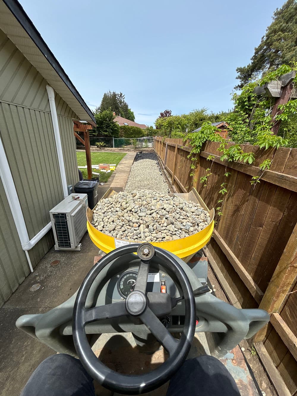 View from a construction vehicle driving on a gravel path beside a wooden fence.