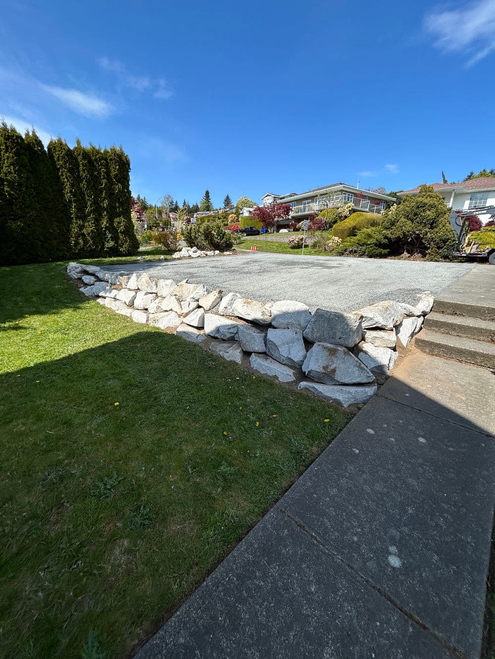Rock wall landscape feature with green grass and blue sky in residential area.