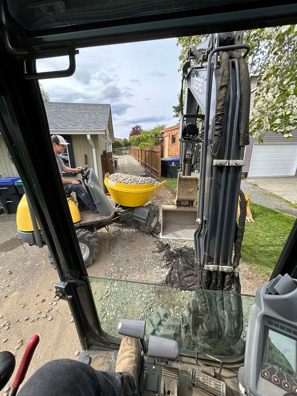 Excavator loading gravel into a yellow wheelbarrow for landscaping project.