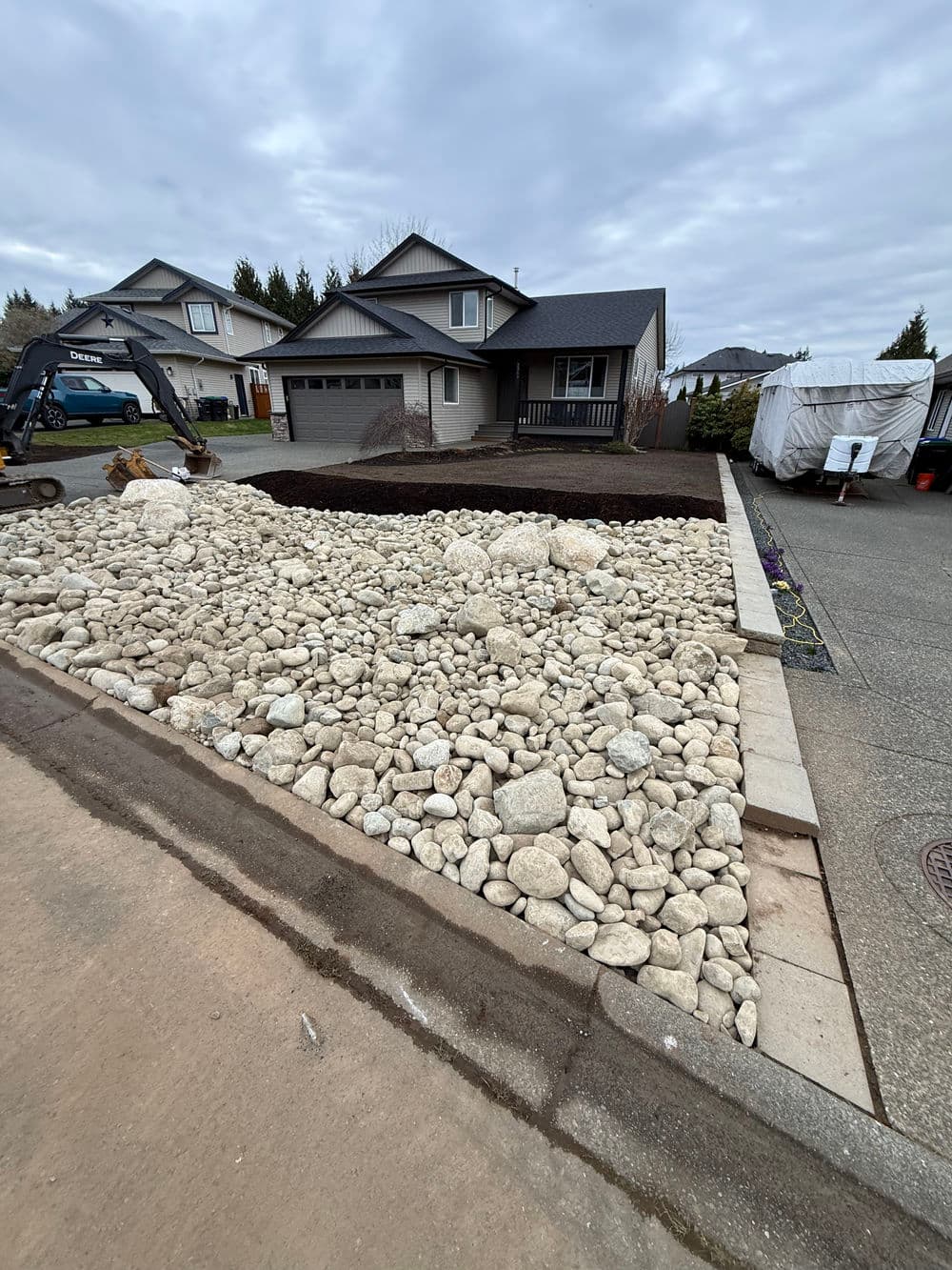 Landscaped front yard with large white stones, mulch area, and a modern home in the background.