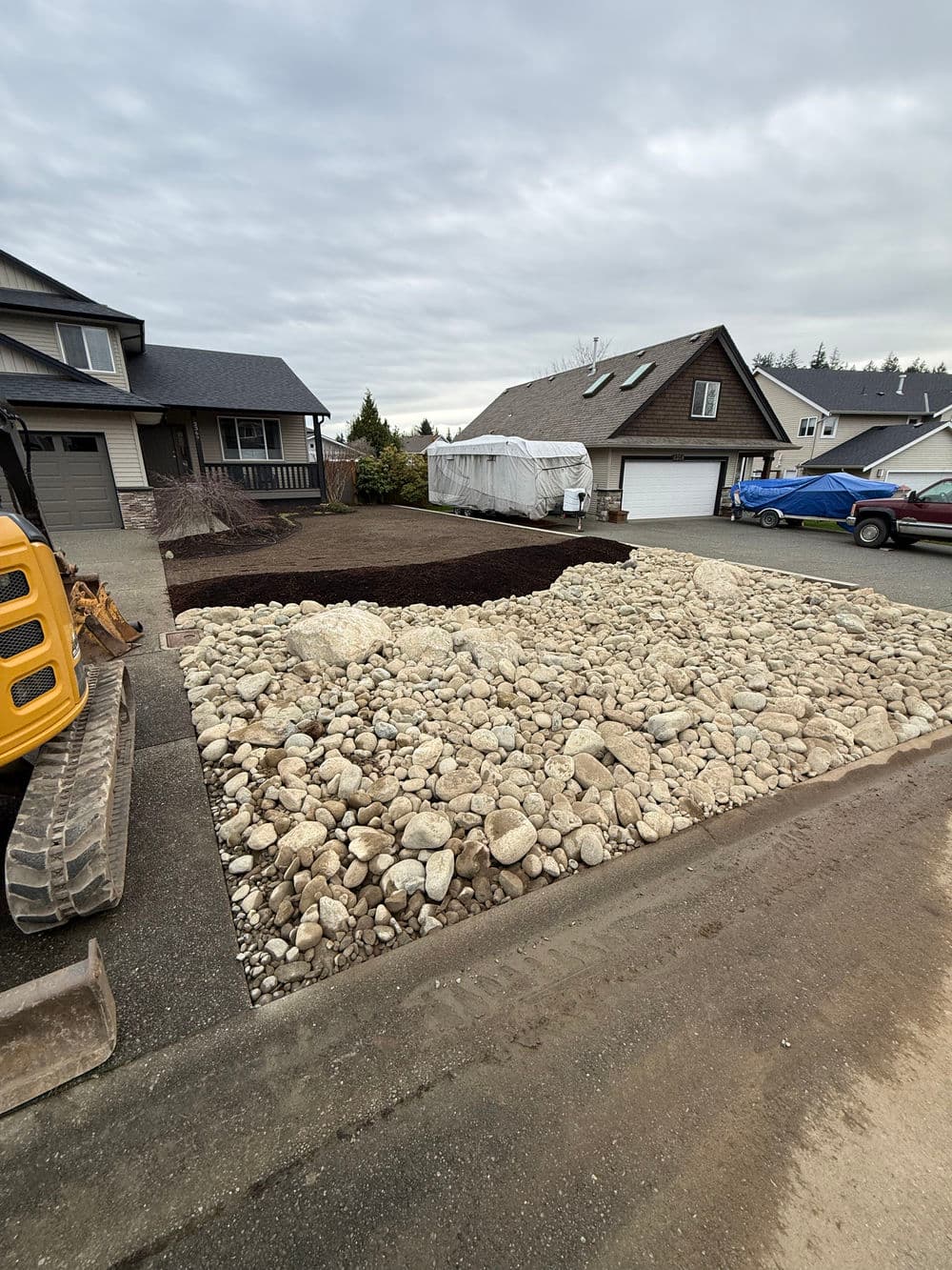 Excavation site with rocks and mulch, residential neighborhood, cloudy sky.