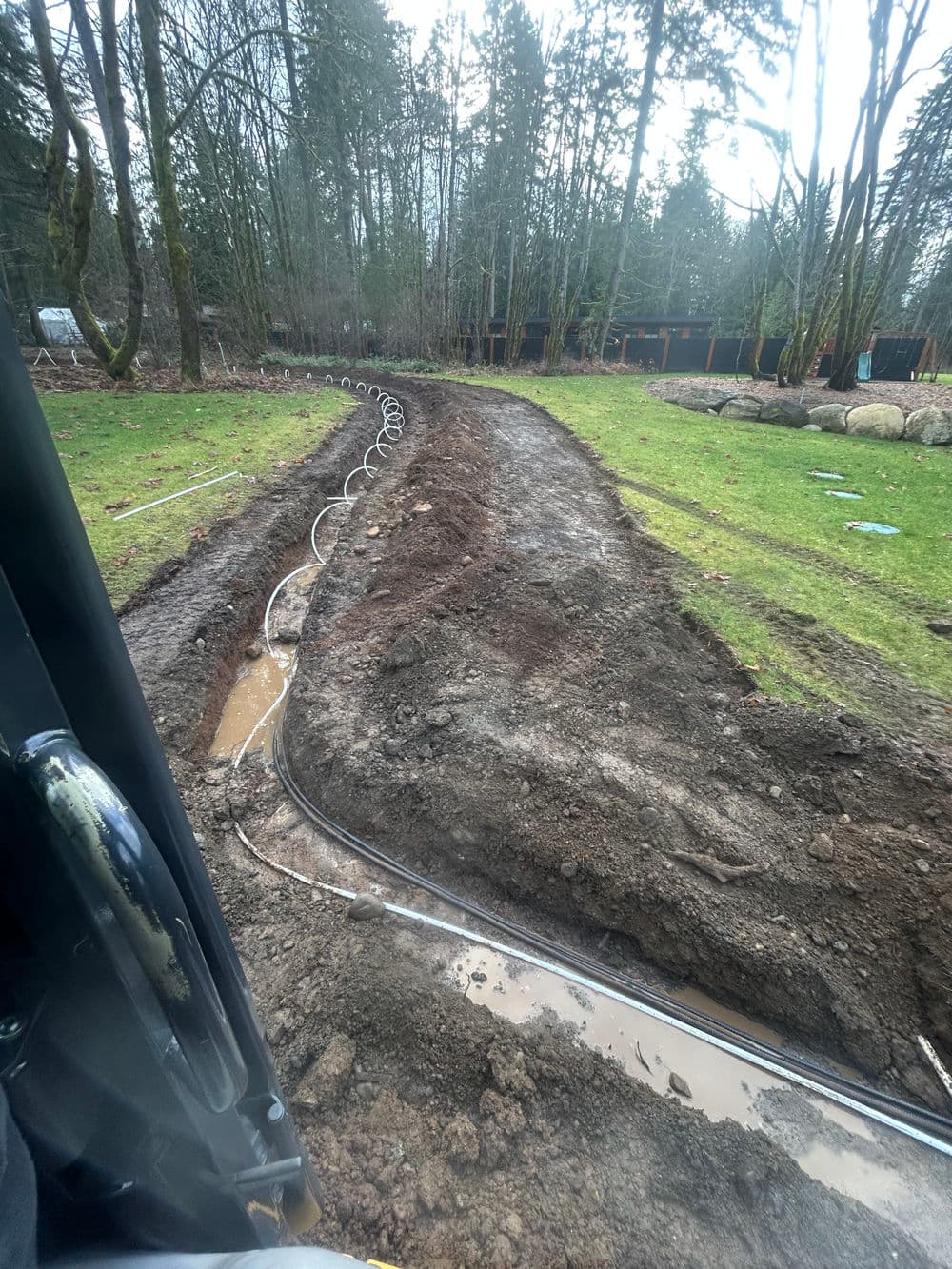 Excavated trench for outdoor utility installation in a forested area with water pooling.