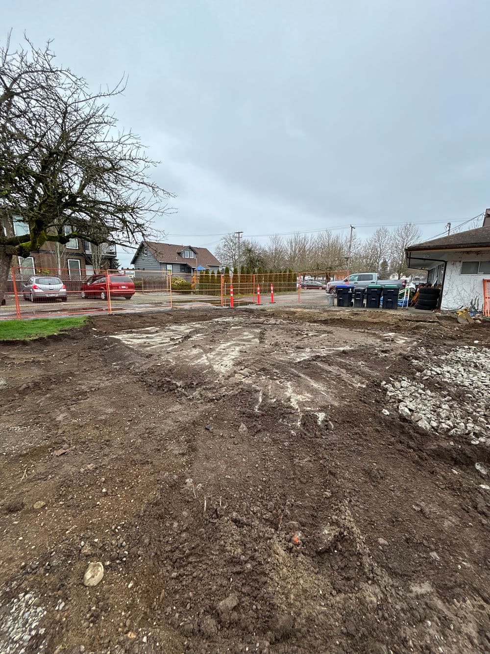 Construction site with cleared ground, barriers, and parked cars in the background.