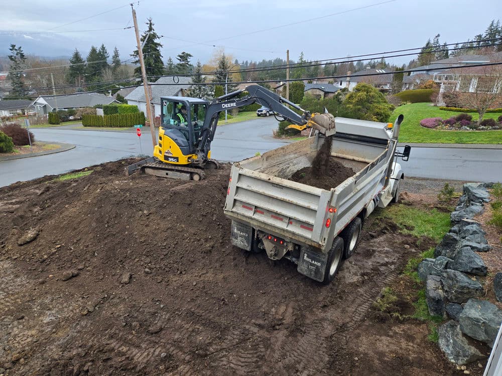 Excavator loading dirt into a dump truck on a residential construction site.
