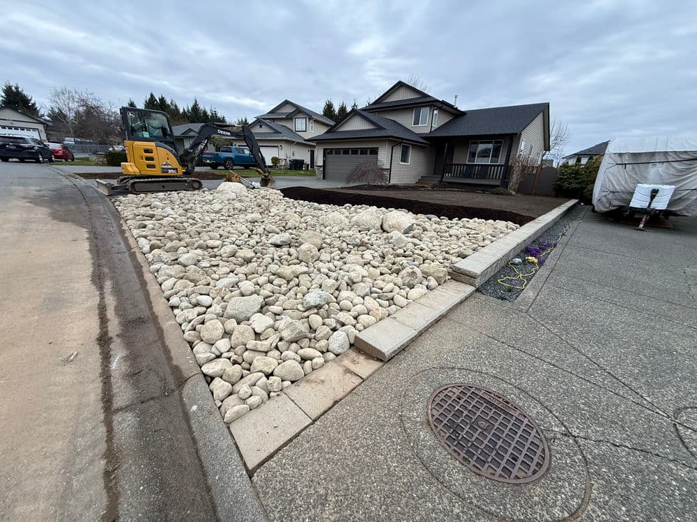 Gravel landscaping project with heavy machinery in residential driveway setting.