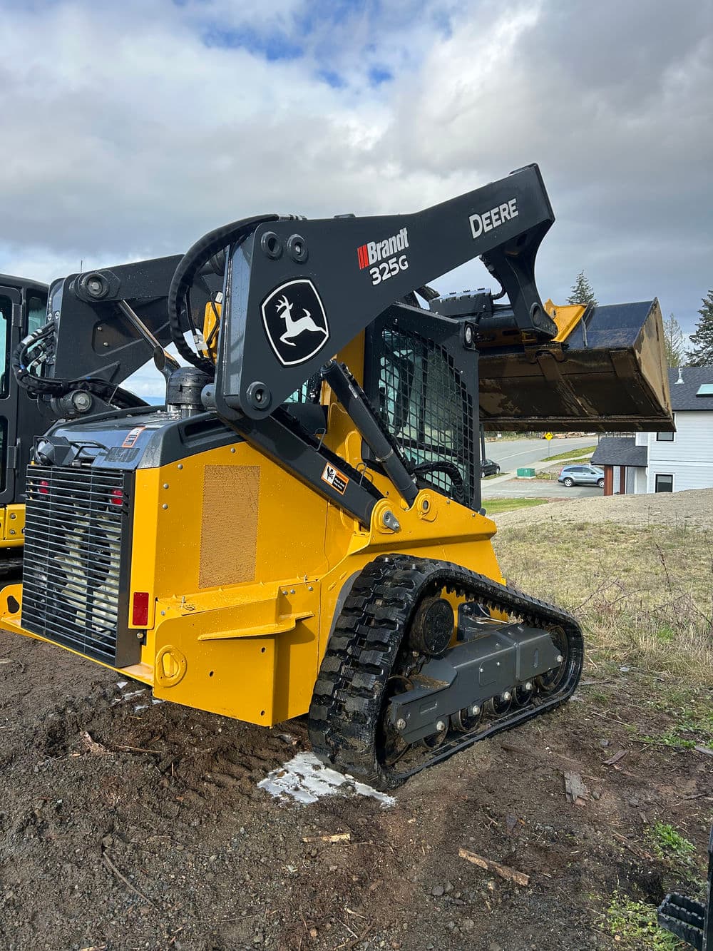 Brandt 325G skid steer loader with tracks, lifting a bucket on a construction site.