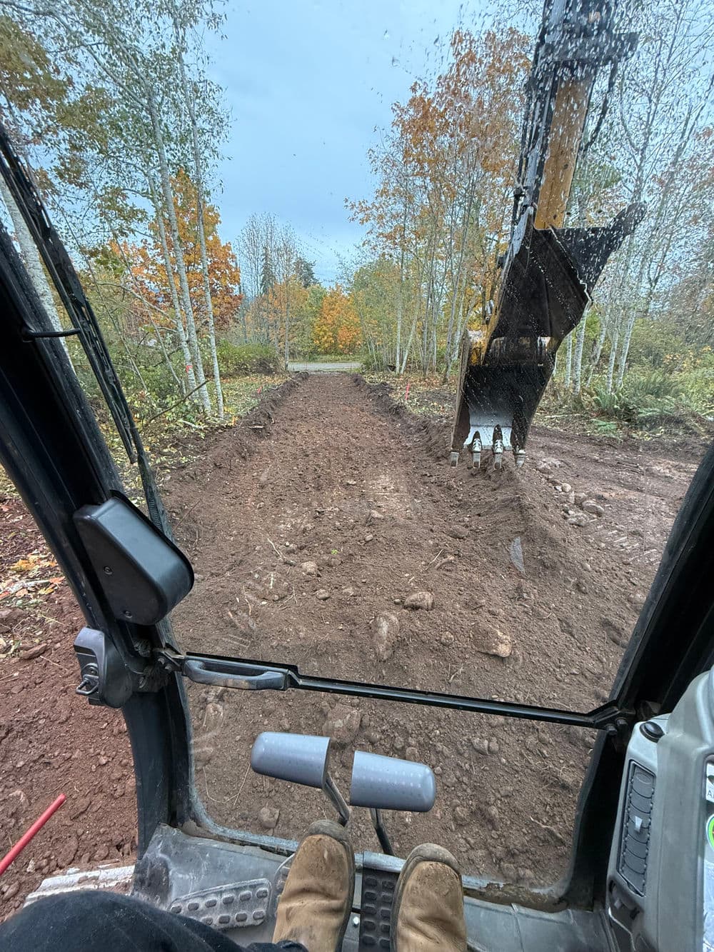 View from a digger's cab showing freshly excavated earth and autumn foliage.