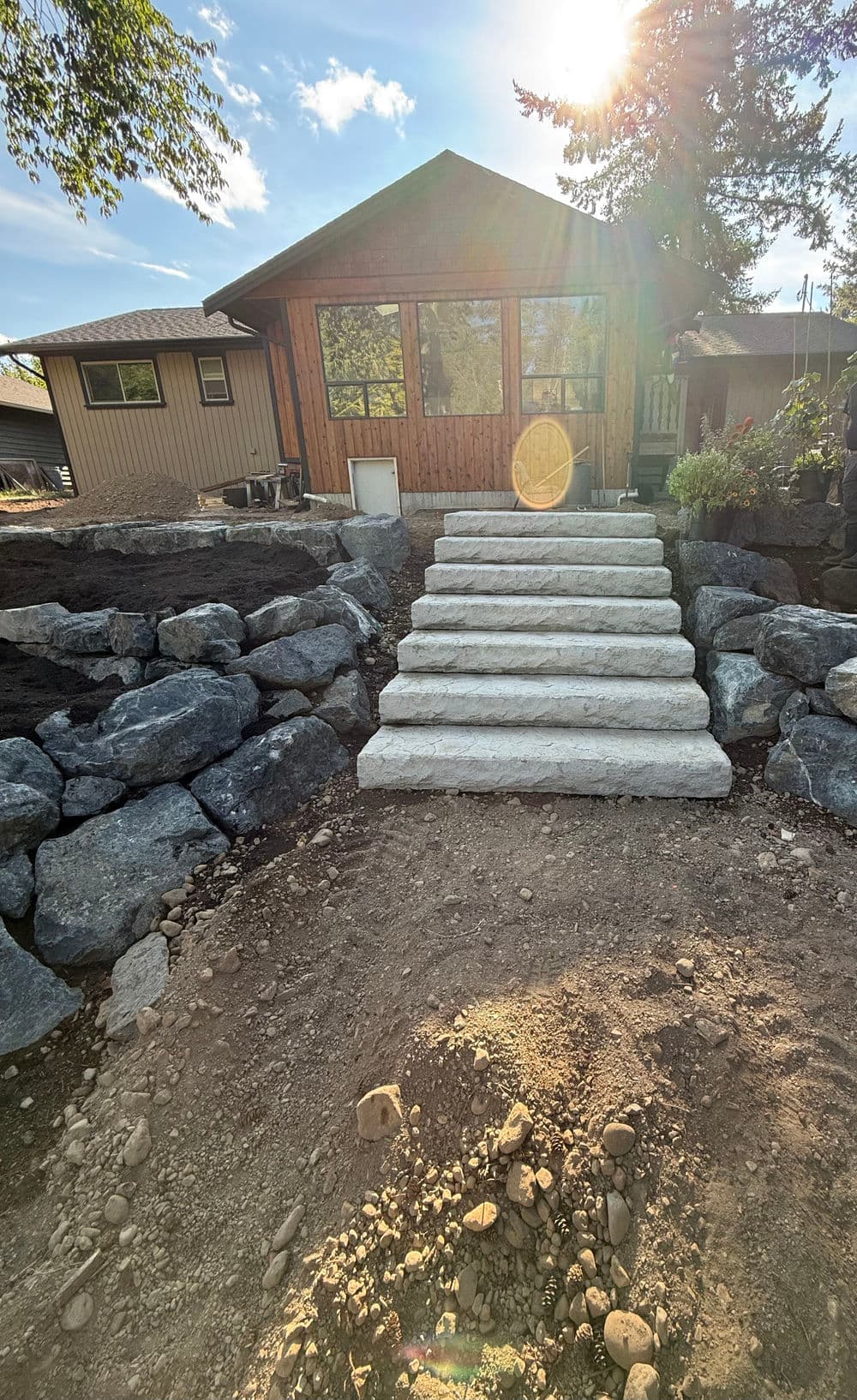 Concrete steps leading to a wooden cabin surrounded by rocks and greenery, under a sunny sky.