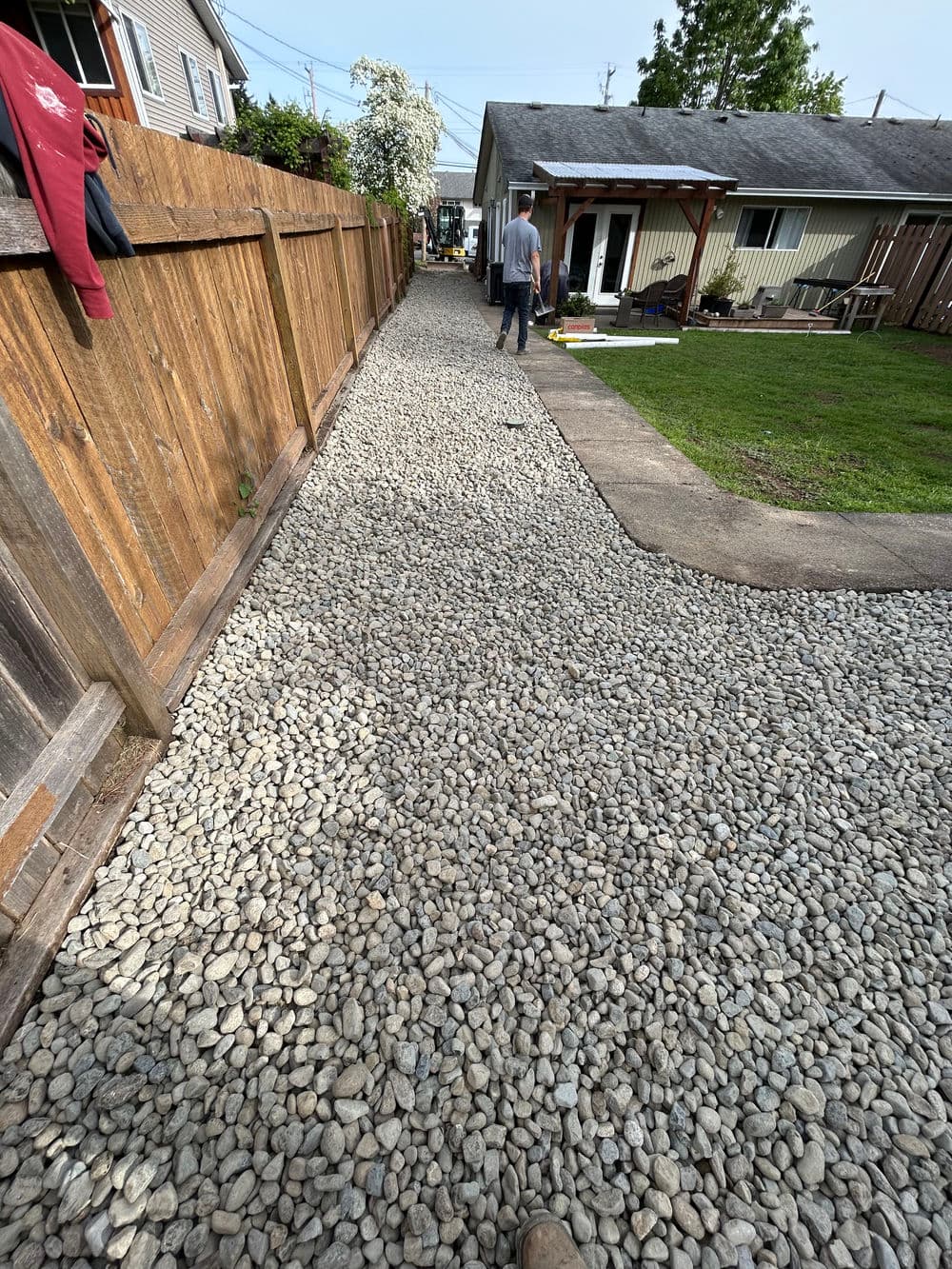 Gravel pathway in backyard with wooden fence and person walking towards house.
