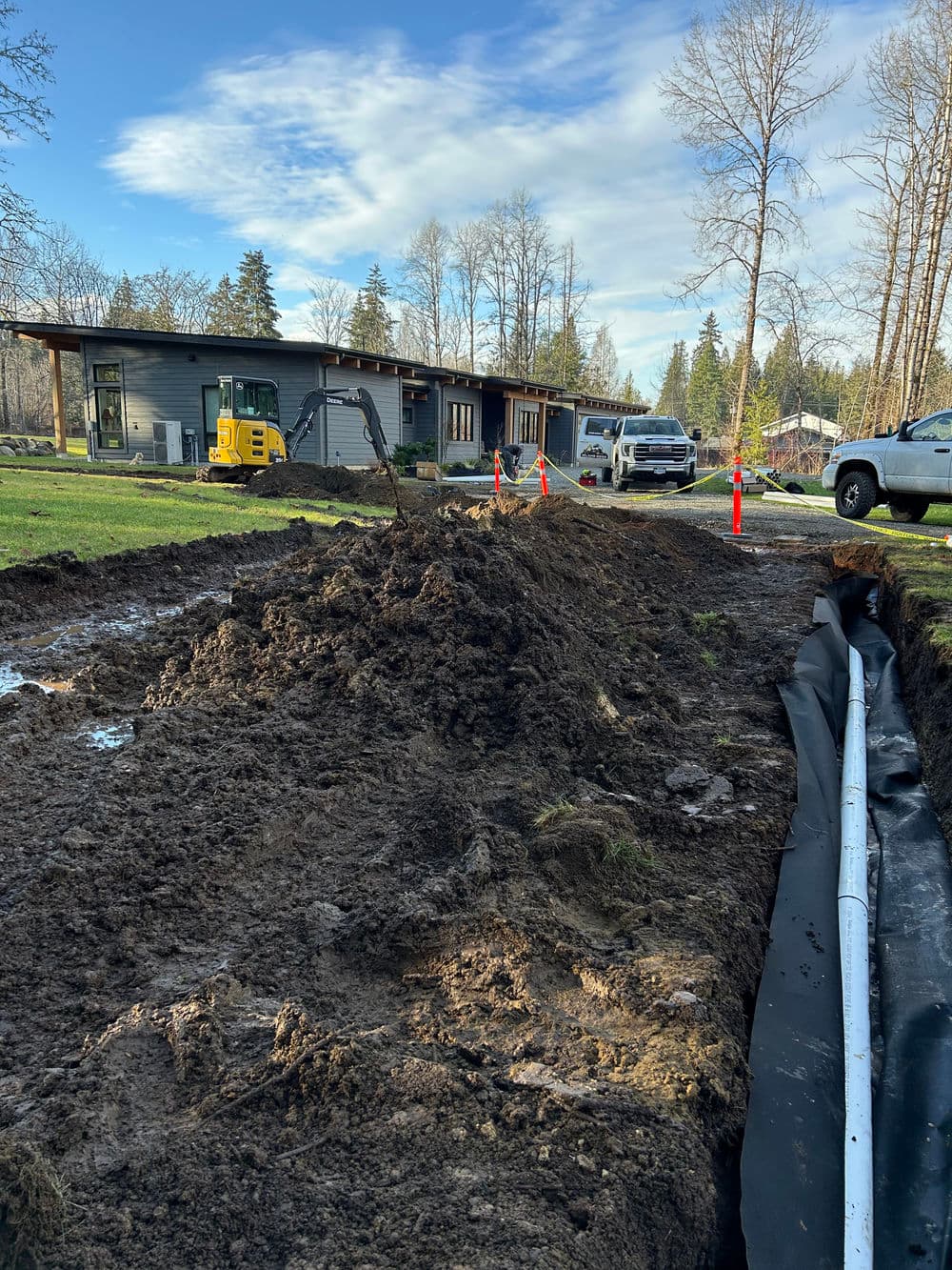 Excavation site with dirt mound, construction vehicles, and a modern house in the background.