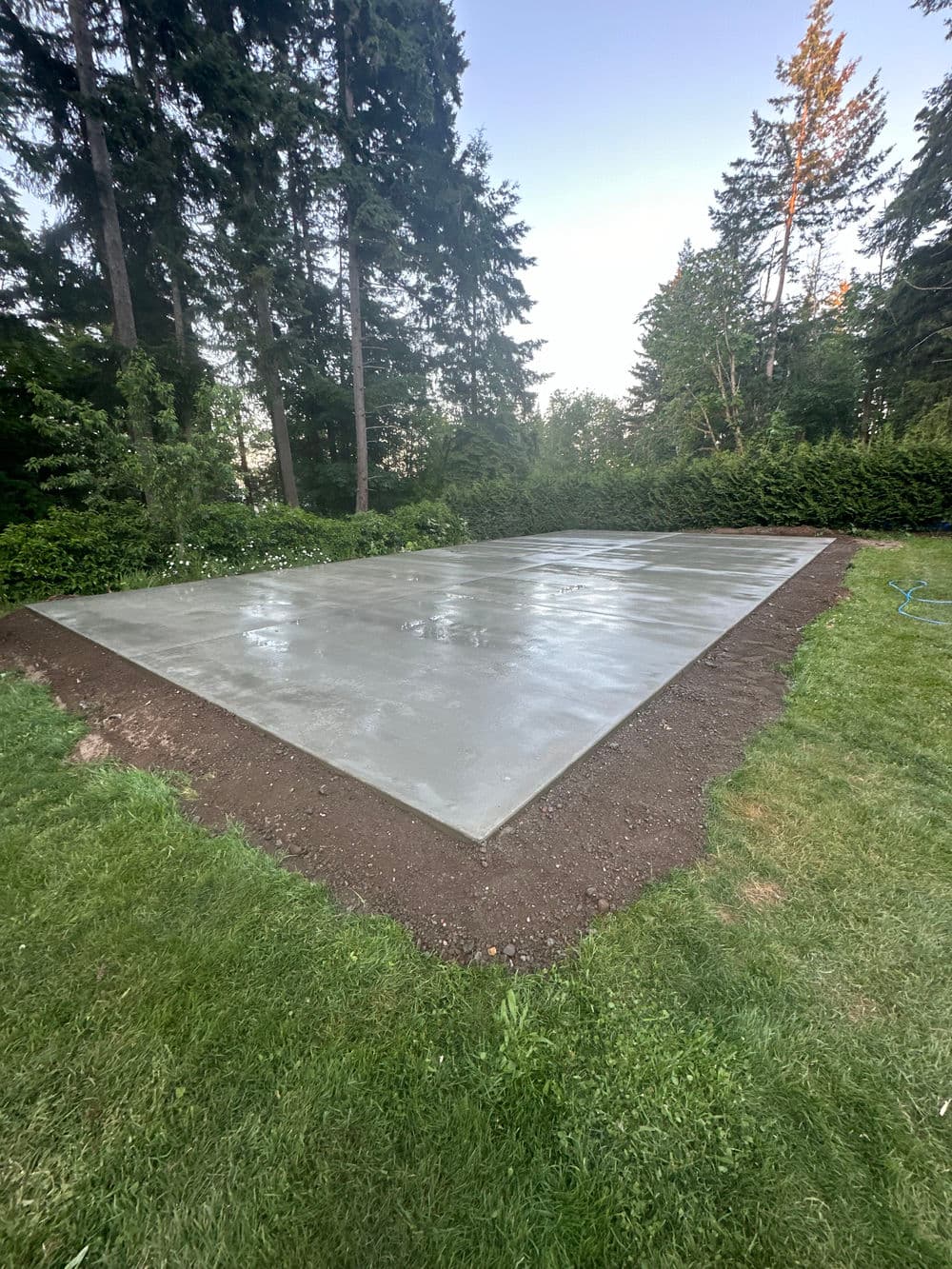 Freshly poured concrete slab in a grassy yard surrounded by trees. Ideal for outdoor projects.