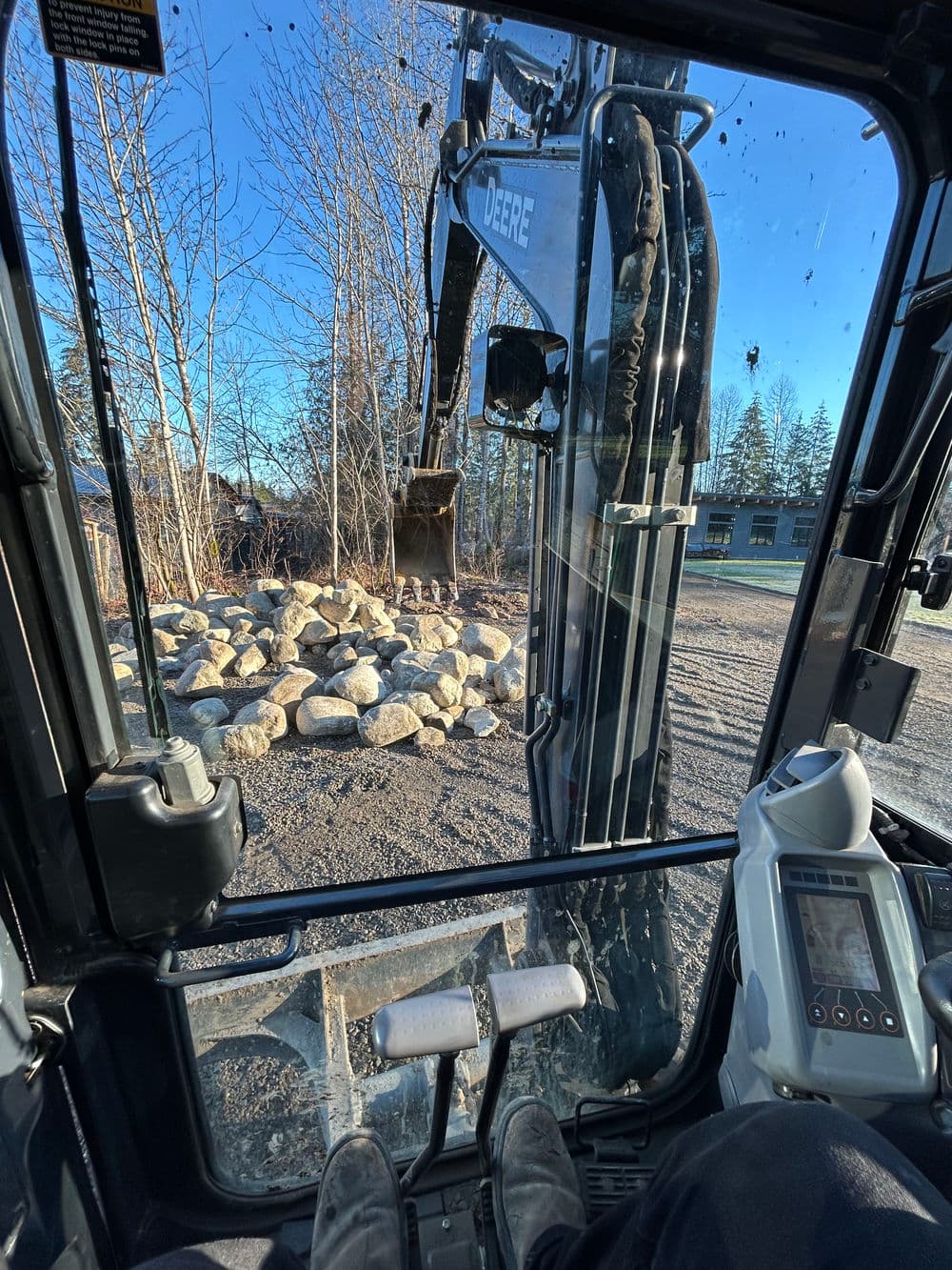 View from an excavator's cabin, focusing on the operating controls and a pile of rocks outside.