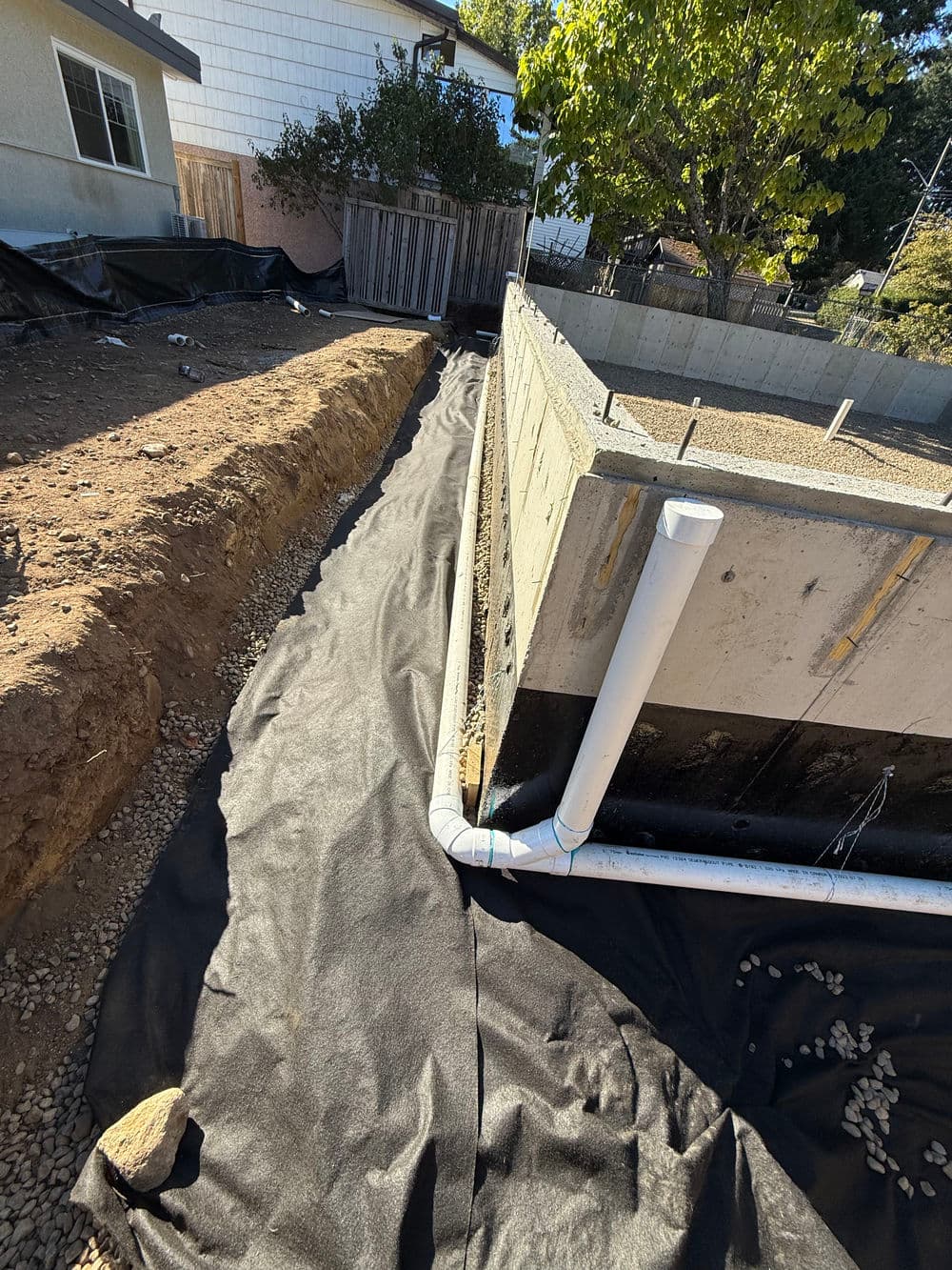 Construction site with black landscaping fabric, gravel, and foundation drainage pipes visible.