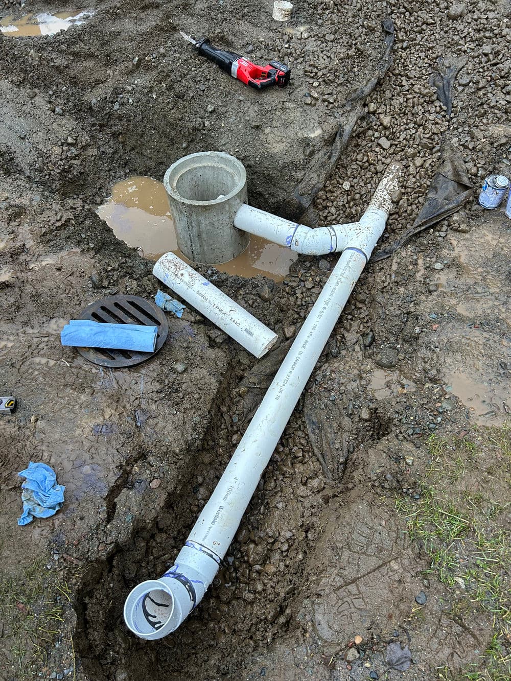 PVC pipes and components in a muddy excavation site for plumbing installation.