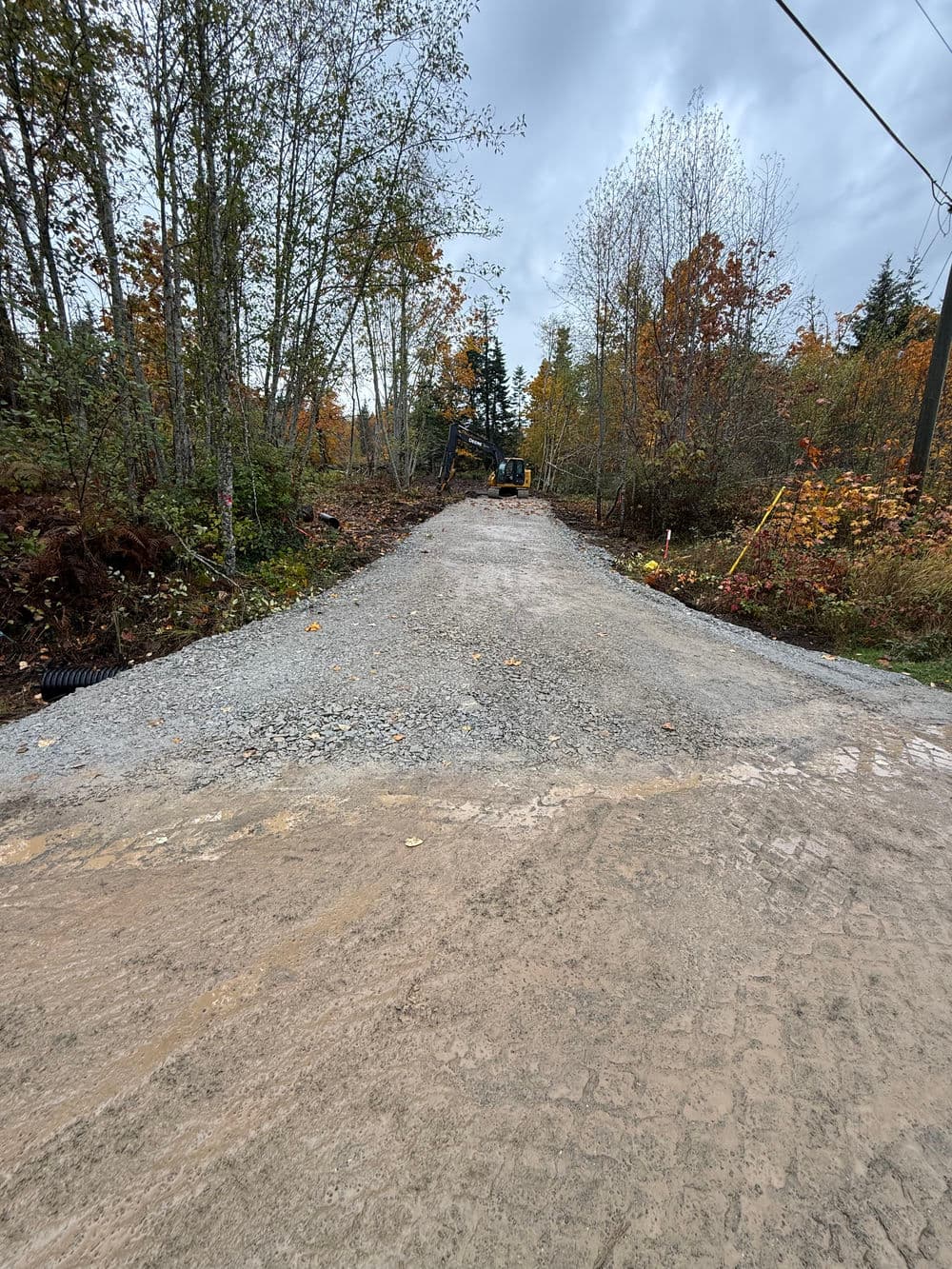 Gravel road under construction surrounded by fall foliage and trees.