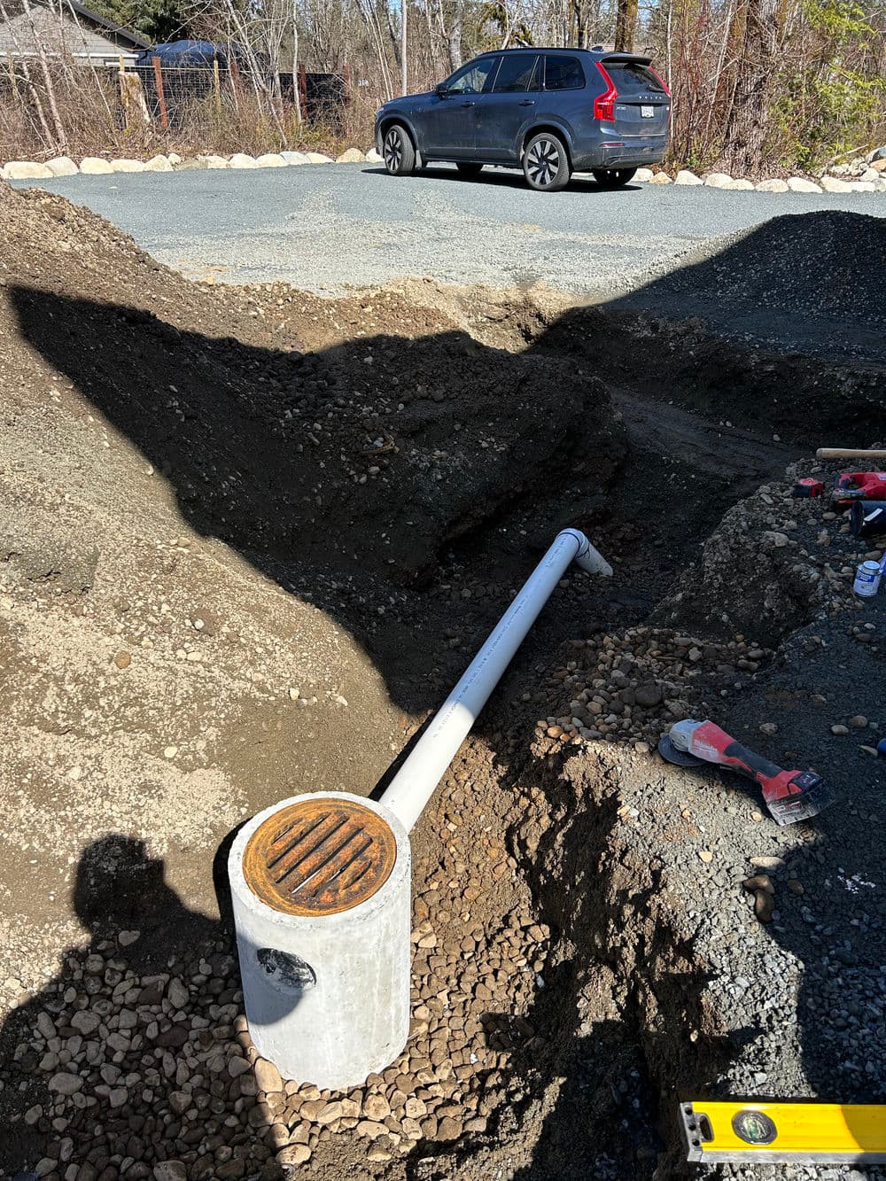 Concrete drainage pipe installation in a gravel trench with a vehicle parked nearby.