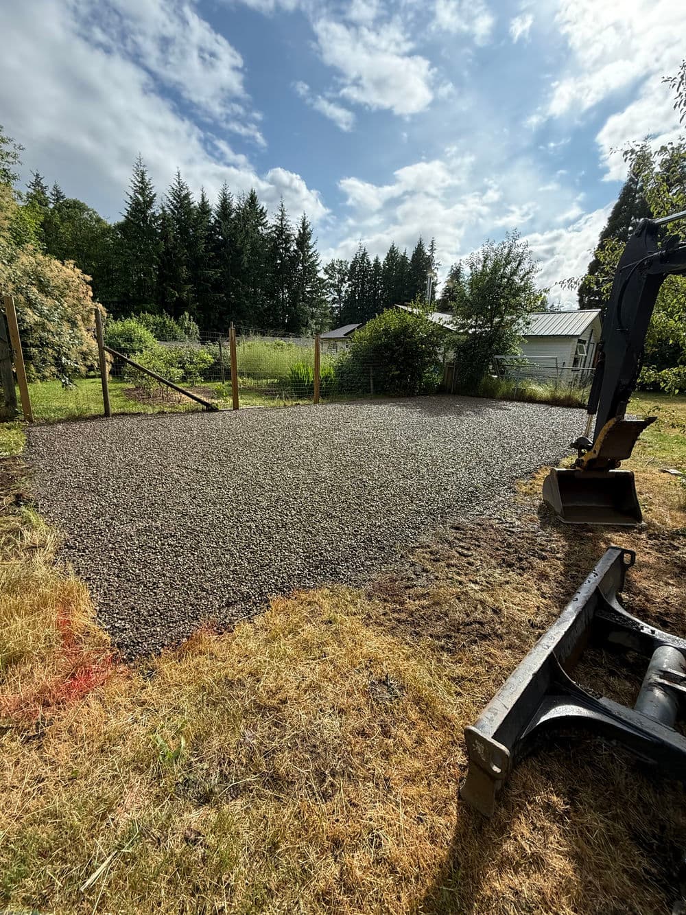 Gravel foundation prepared for landscaping in sunny backyard with trees and equipment nearby.