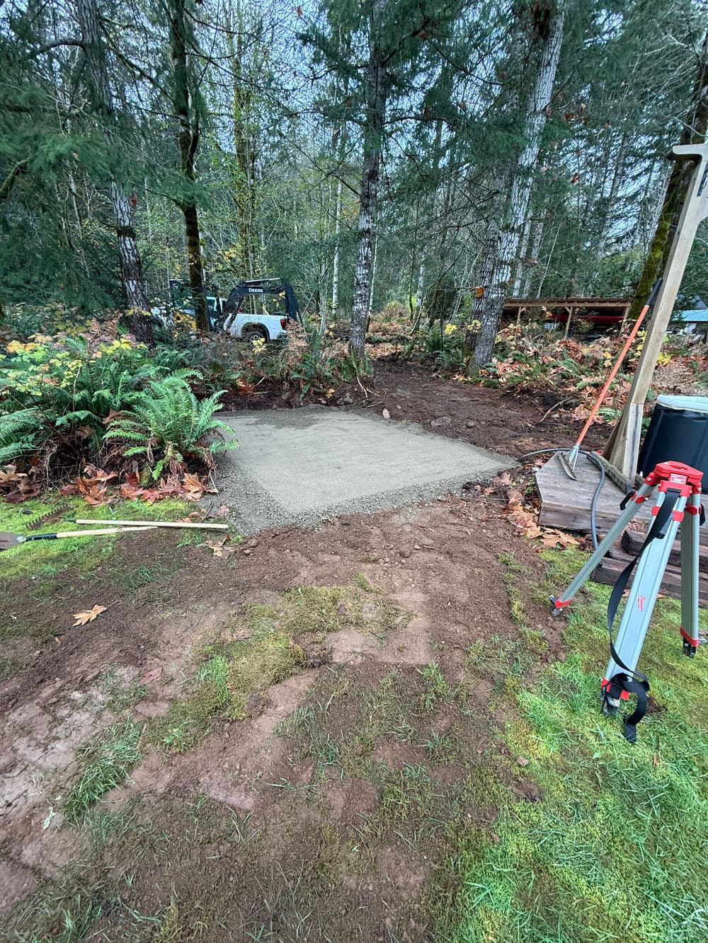 Concrete slab foundation construction amid trees and ferns in a natural landscape.