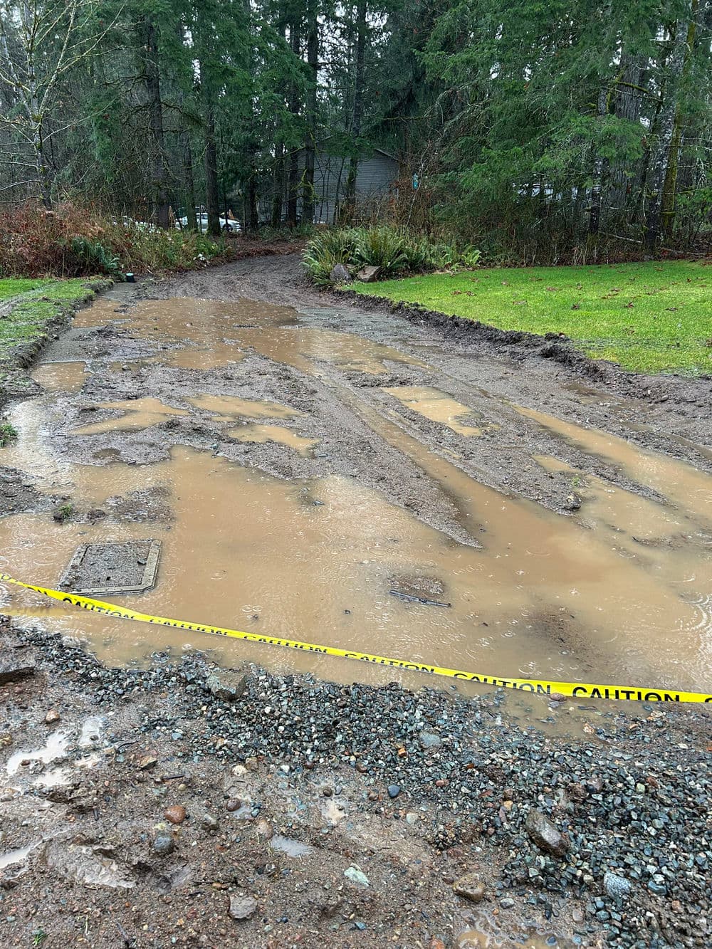 Mud and water-filled area with caution tape, surrounded by greenery and trees.