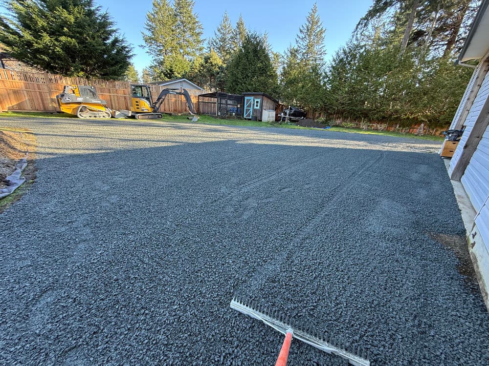 Gravel driveway installation with machinery in a residential yard under clear blue sky.