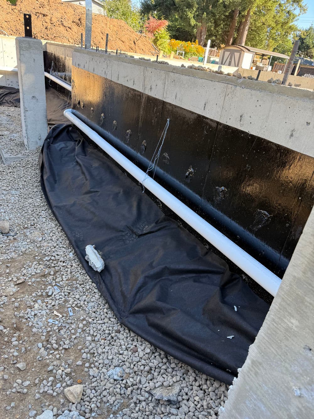 Construction site with exposed foundation, drainage pipe, and protective black sheeting.