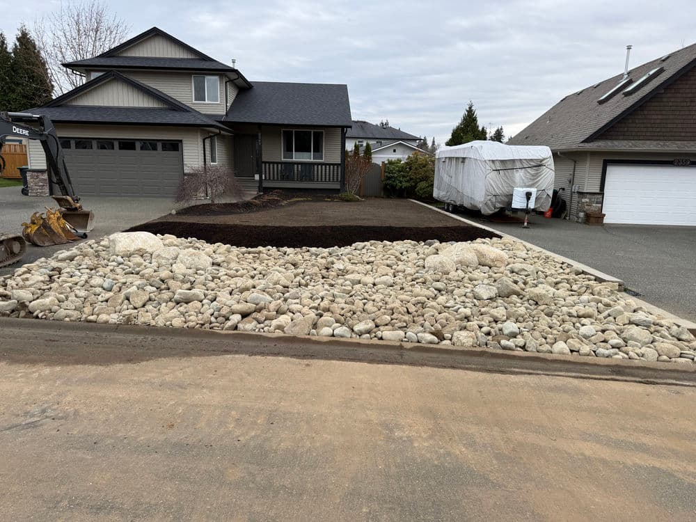 Residential landscape transformation with gravel and mulch in front yard, equipment nearby.