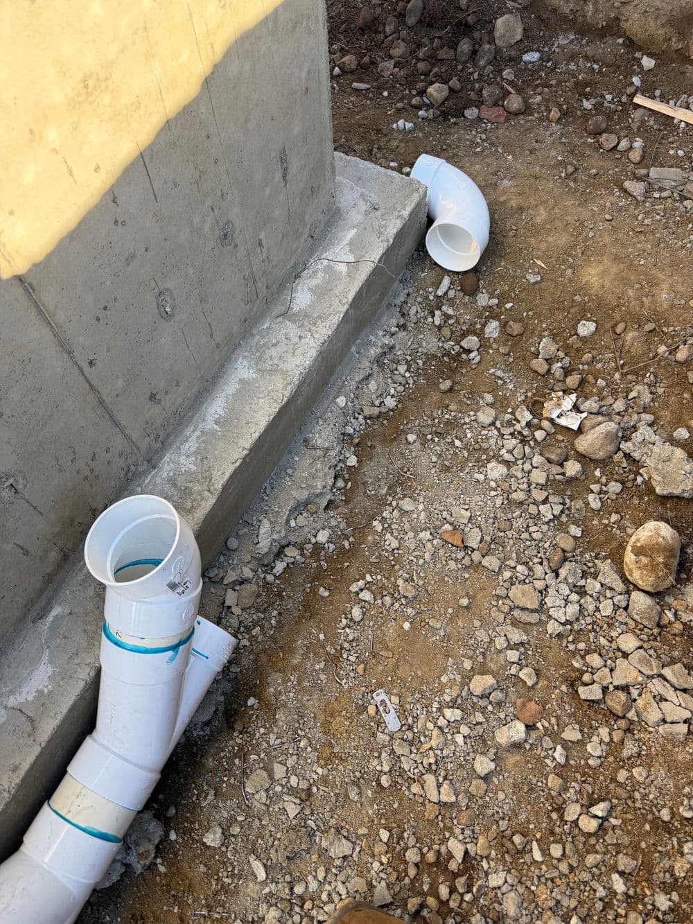 PVC pipes arranged beside a concrete foundation, on a gravel and dirt surface.