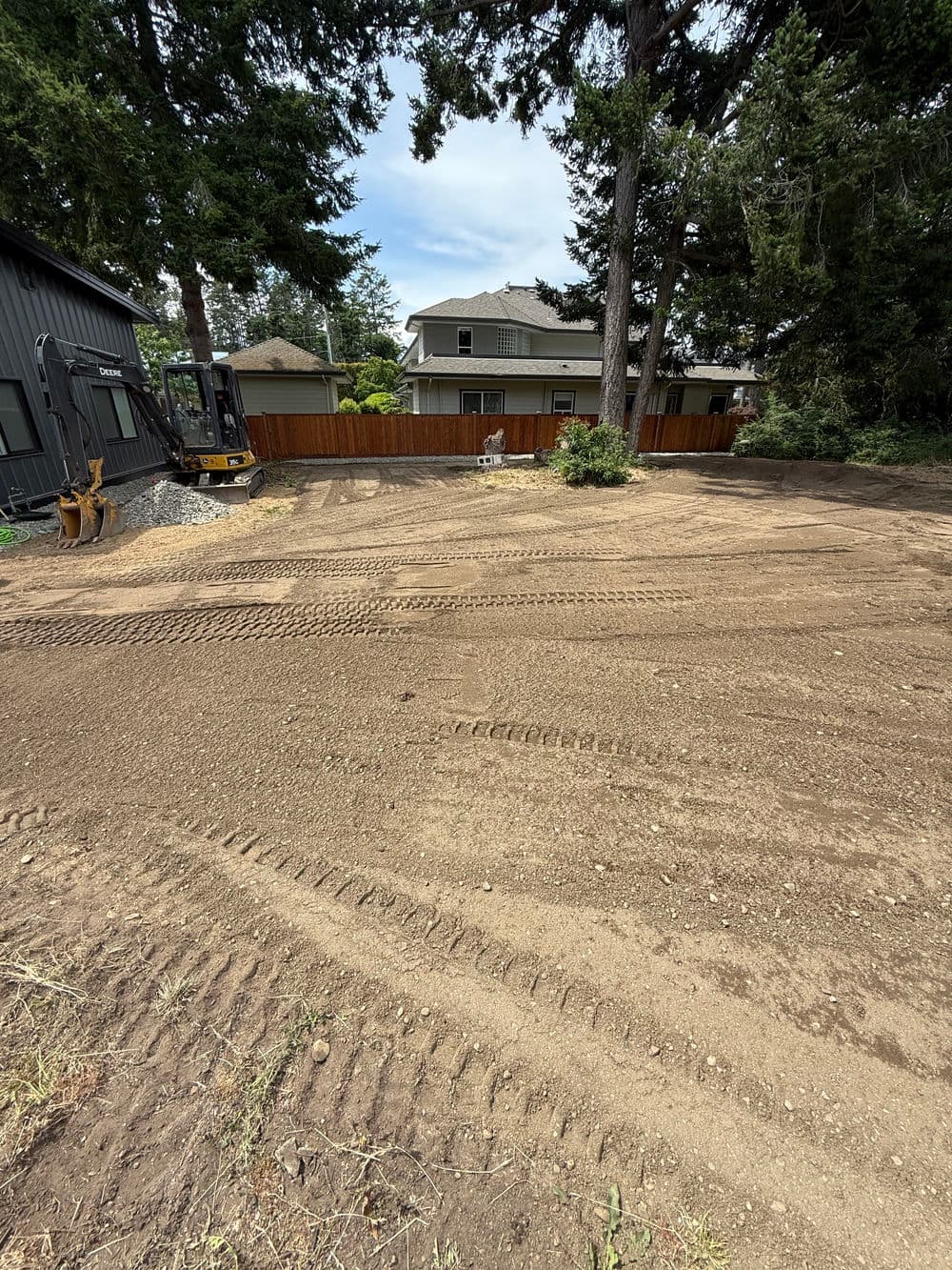 Excavated backyard with tire tracks, trees, and homes in the background. Ideal for landscaping.