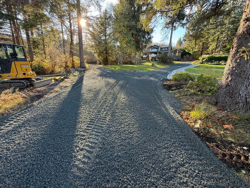 Newly paved gravel driveway leading to a house, surrounded by trees and natural landscaping.