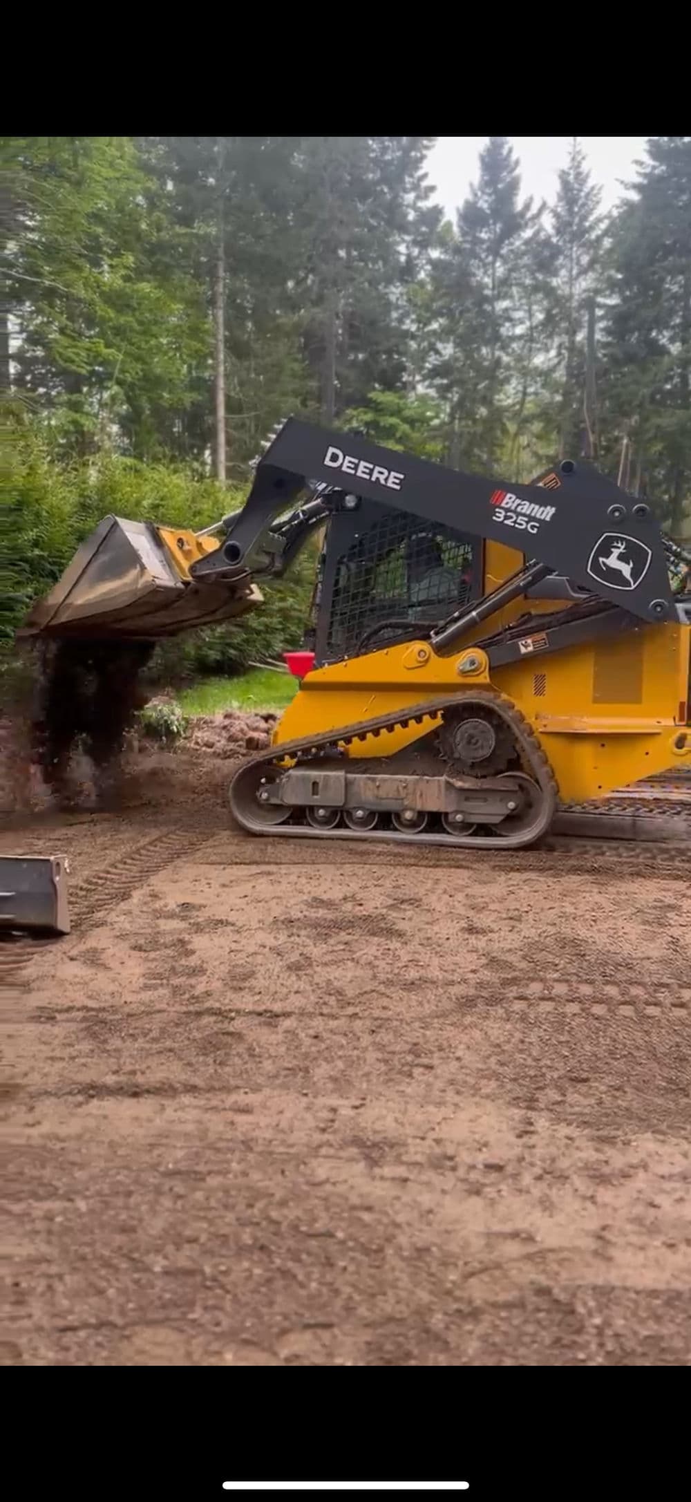 John Deere 329E skid steer loader digging and transporting soil on a construction site.