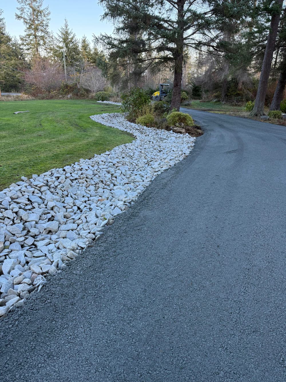 Curved rock border along a driveway with green grass and trees in the background.
