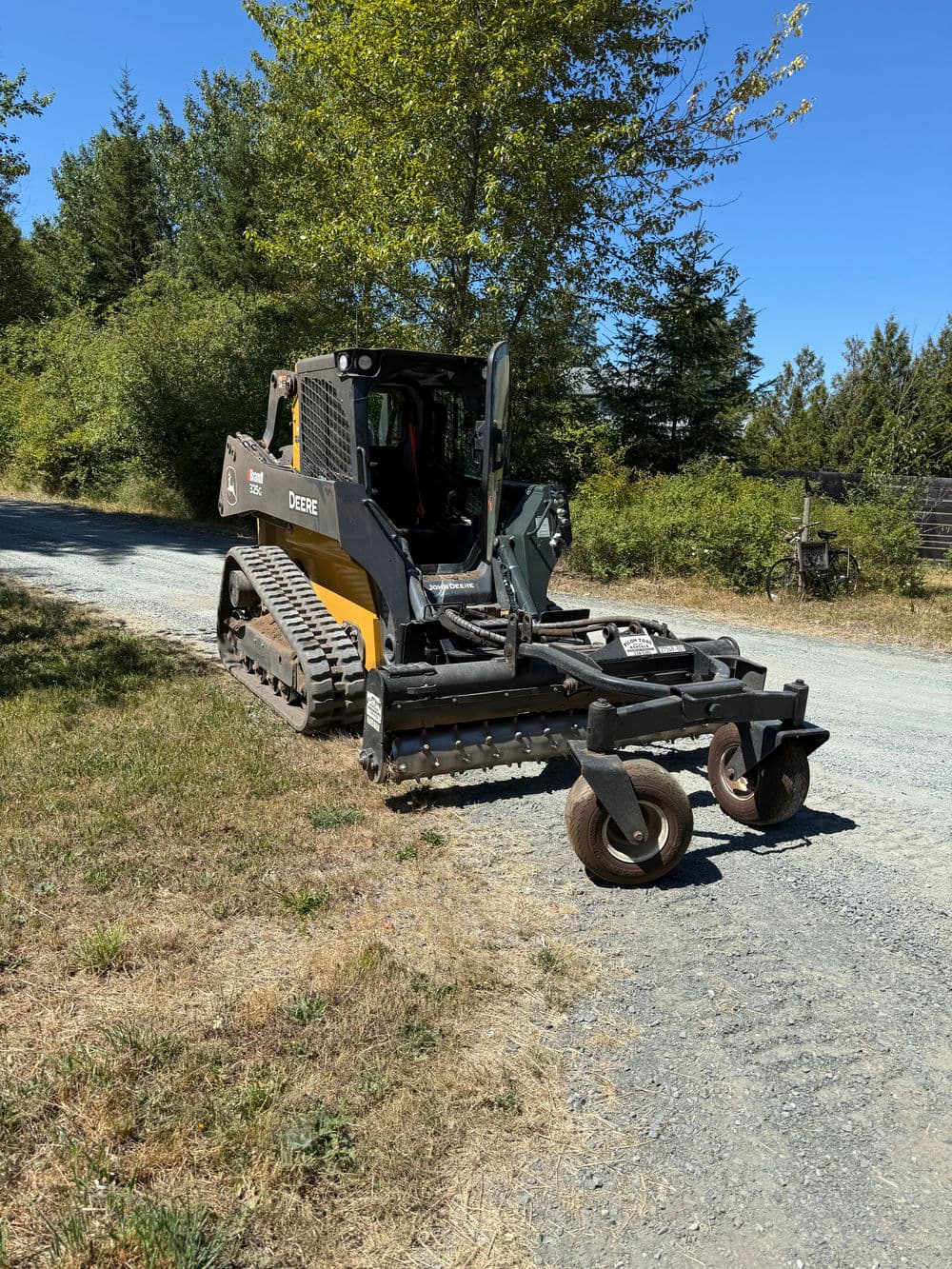John Deere dozer on a gravel road surrounded by trees and greenery.