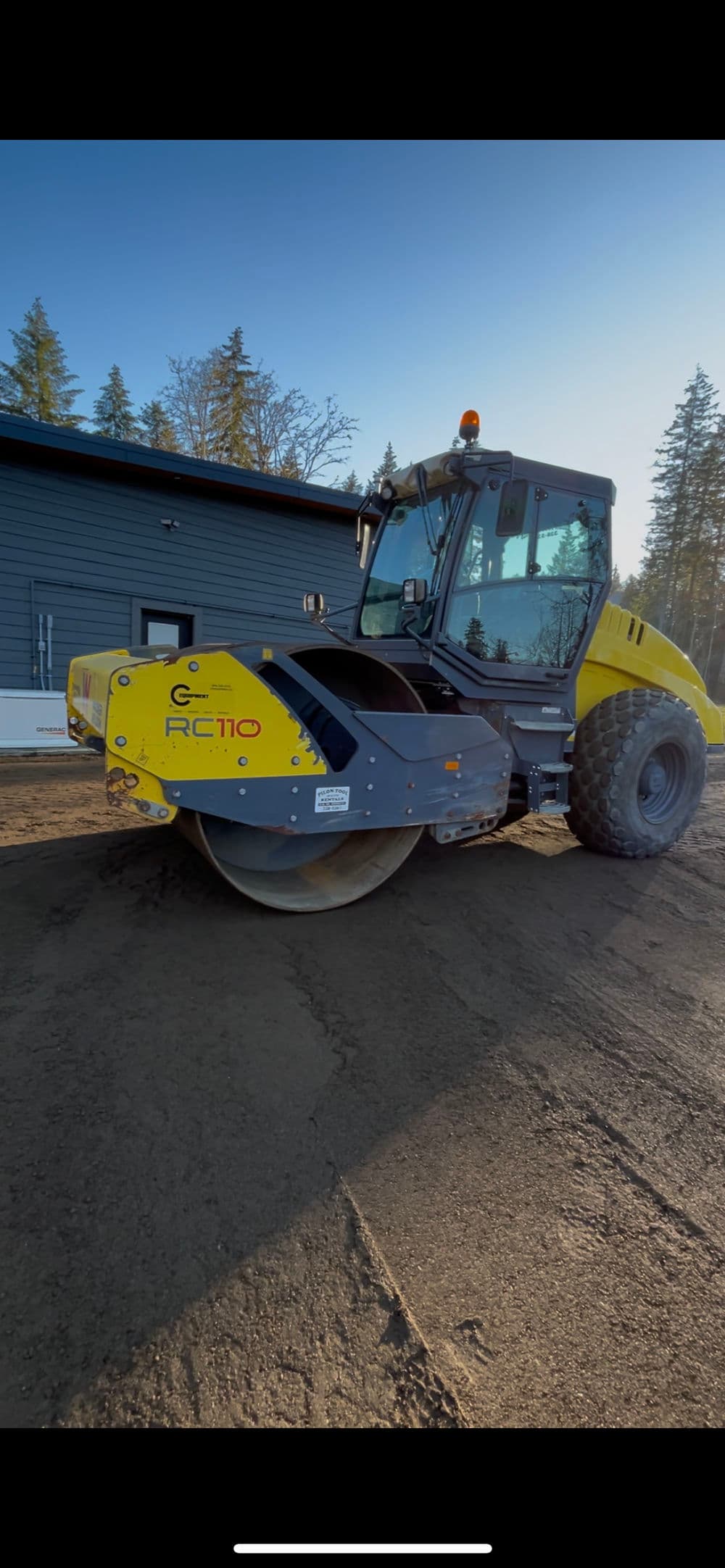 Yellow and gray RC110 road roller on a construction site with a modern building in background.